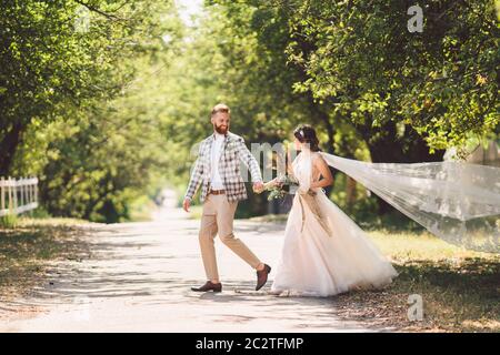 Bella foresta di legno di coppia di nozze. Sposa e sposo, seguimi, coppia sposata, donna in abito da sposa bianco e velo. Rustica Foto Stock