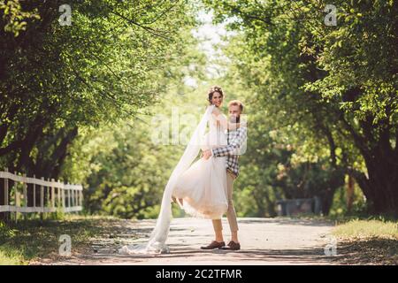 Felice sposo alza sposa nel parco estivo. Uomo alzato e abbraccio donna alle braccia. Coppia appena sposata nel parco. Solo matrimonio Foto Stock