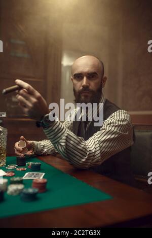 Giocatore di poker con bearded e sigaro che gioca nel casinò. Giochi di dipendenza casuale. Uomo svaghi in casa gioco d'azzardo Foto Stock