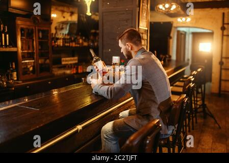 Uomo con bottiglia di alcol bevande bevande al bar in legno contatore. Il cliente di svaghi in pub, maschio persona potrete rilassarvi nel ristorante Foto Stock