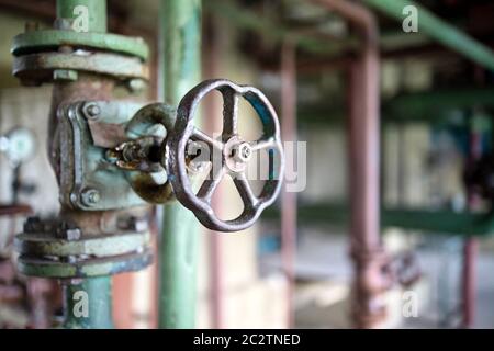 Flange per tubazioni industriali primo piano di valvole e volantino, sfocatura dello sfondo delle tubazioni industriali. Vecchie apparecchiature di controllo arrugginite, abbandonate industria di impianti Foto Stock