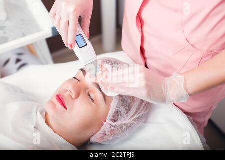 Medico con scraper ecografico che fa procedura di pulizia ecografica del viso. Clinica cosmetologica. Trattamento per la cura della pelle. Cosmetologia. Foto Stock