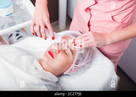 Medico che fa la procedura medica con scraper ultrasonico. Pulizia a ultrasuoni del viso. Cosmetologia. Assistenza sanitaria. Foto Stock