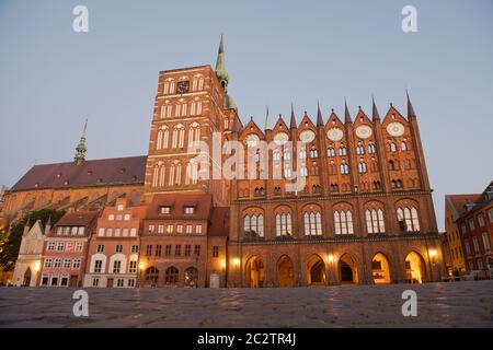 Stralsund, Germania. 15 giugno 2020. Vista della chiesa di San Nikolai e del municipio (r) all'ora blu. I dischi di gioielleria parzialmente placcati in oro, circa 80 kg, sono stati realizzati intorno al 1880 secondo il modello tardo medievale. Si presume che i dischi delle stelle simboleggino il regno dei cieli, che come ordine divino si trova sopra l'ordine terreno, umano - il municipio con il suo consiglio. Il municipio di Stralsund, patrimonio dell'umanità, è uno dei più importanti edifici secolari anseatici della regione del Mar Baltico. Credit: Stefan Sauer/dpa-Zentralbild/dpa/Alamy Live News Foto Stock