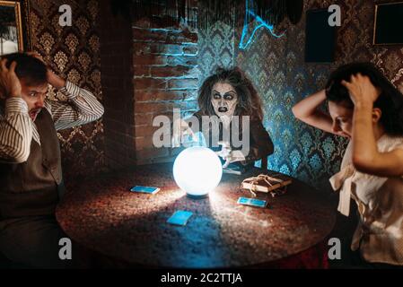 Strega legge scary magic spell su una sfera di cristallo, giovani in genere horror in seance spirituale. Femmina chiamate foreteller gli spiriti Foto Stock