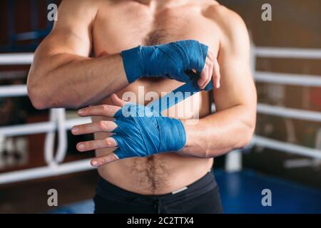 Primo piano di mano di pugile di forza che tira la bendatura prima della lotta o l'addestramento. Anello di boxe sullo sfondo. Foto Stock