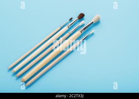 Spazzole per imbutitura con vernici in legno naturale e lana su fondo blu. Foto Stock