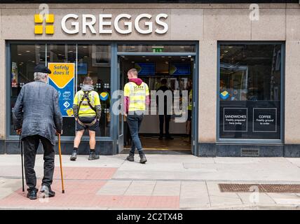 Haddington, East Lothian, Scozia, Regno Unito, 18 giugno 2020. Riapertura delle aziende: Con la facilità delle restrizioni di blocco, le aziende locali possono riaprirsi. Alcuni negozi di Greggs in Scozia riaprono oggi, tra cui quello di Market Street. Due operai in giubbotti gialli si accodano fuori dal negozio di sandwich da asporto mentre un anziano con un bastone cammina verso il negozio Foto Stock