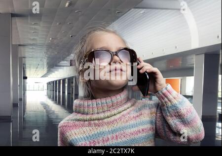 Carino bambina in occhiali da sole parla al telefono Foto Stock