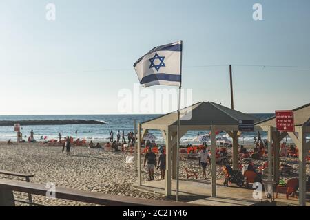 Tel Aviv / Israele-13/10/18: Turisti che riposano su una spiaggia sul Mediterraneo a Tel Aviv; bandiera nazionale israeliana che svetta in primo piano Foto Stock