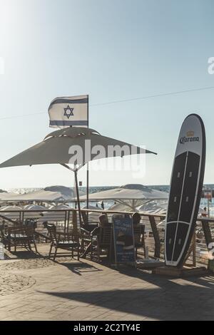 Tel Aviv / Israele-13/10/18: Turisti che riposano sotto un ombrello su una spiaggia sul Mediterraneo a Tel Aviv; longboard in primo piano, Israeli n Foto Stock