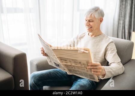 Uomo adulto seduto sul divano e la lettura quotidiano a casa. Maschio maturo persona si rilassa in poltrona Foto Stock