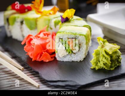 Gustoso sushi set. Piatti tradizionali giapponesi. Panini di riso. Ripieni di pesce, verdure e formaggio. Archiviato su una tavola di metallo nero con zenzero e wasab Foto Stock