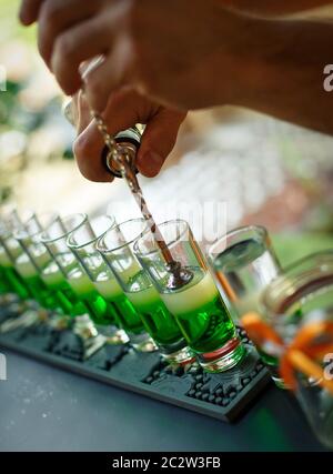 Barista che fa colpi di alcool al bar. Barman prepara cocktail verdi per una festa. Esperto barman che mescola cocktail colorati. Foto Stock