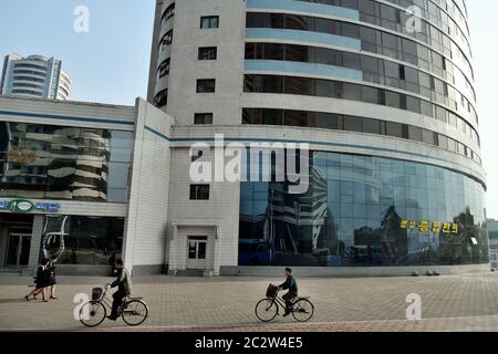 Pyongyang, Corea del Nord - 30 aprile 2019: Un uomo in bicicletta lungo una strada, le studentesse vanno a scuola la mattina presto Foto Stock