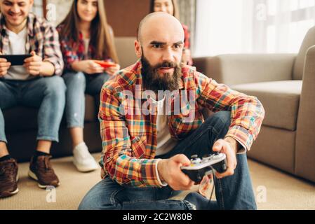 Amici sorridente con il joystick riproduce console tv a casa. Gruppo di giocatori con joypads giocando videogioco, maschio e femmina con giocatori gamepad Foto Stock