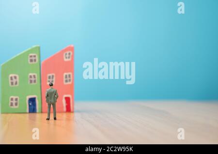 Figura uomo d'affari in piedi davanti a colorato del modello di casa di legno sul tavolo e spazio di copia per il testo. Concetto di investimento in costruzione di casa Foto Stock