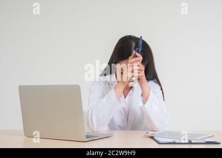 Giovane donna asiatica dottore seduto sulla scrivania, lei sembra infelice e stanca a causa di lavoro eccessivo, concetto di stressato e responsabilità medico, trattare Foto Stock