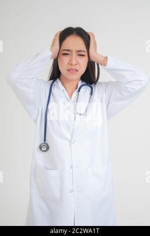 Giovane donna asiatica medico in piedi e tenendo le mani in testa a causa di mal di testa, sembra infelice e stanca a causa di lavoro eccessivo, concetto di stressato Foto Stock
