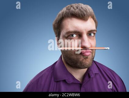 Strano uomo barbuto detiene una matita con il suo naso e le labbra Foto Stock