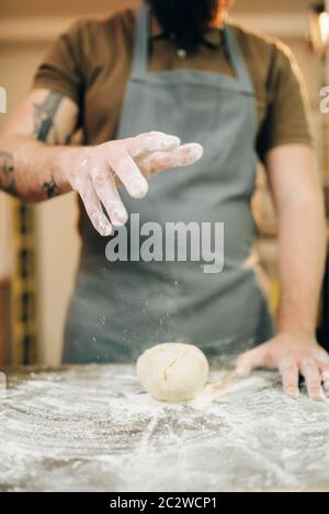 Pasta fresca cucina, cuoco grembiule rende la pasta. L'uomo preparare spaghetti di legno sul tavolo da cucina Foto Stock