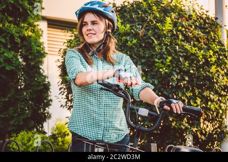 Ritratto di un cellulare allegro ragazza tenuta. Felice studente sorridente che usa l'app per la condivisione delle biciclette su smartphone all'aperto. Vita cittadina Foto Stock