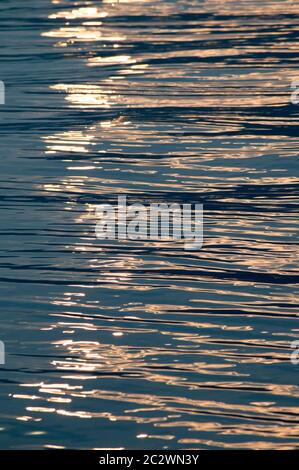Luce del tramonto che si riflette sulla superficie ondulata dell'acqua Foto Stock