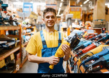 Costruttore maschile scelta della smerigliatrice angolare presso lo scaffale in negozio di hardware. Costruttore in uniforme guardare la merce in negozio fai da te Foto Stock