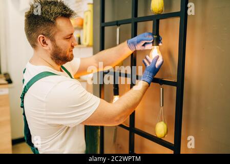 Elettricista in uniforme cambia la lampadina, handyman. Lavoratore professionale effettua riparazioni intorno alla casa, servizio di riparazione a casa Foto Stock