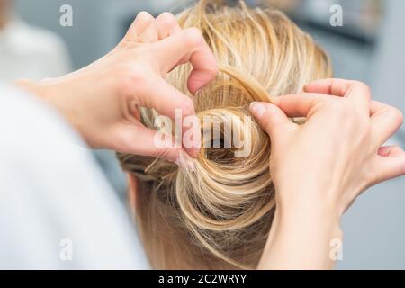 Primo piano vista posteriore del parrucchiere che fa acconciatura per capelli lunghi di donna bionda. Foto Stock