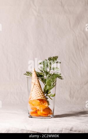 Sorbetto al gelato di carote vegetali vegane con cono di waffle su fondo tessile beige.Healthy mangiare concept.Fashion composizione alimentare Foto Stock