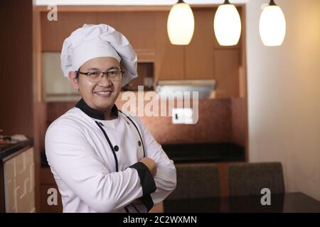 Ritratto di felice chef asiatico sorridente con le braccia incrociate, chef in cucina, chef di successo nel settore dei ristoranti Foto Stock