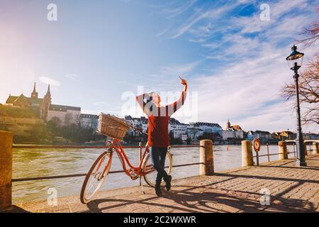 Una bella giovane donna con una bicicletta rossa retrò sta facendo una foto di se stessa nella città vecchia d'Europa sul fiume Reno emban Foto Stock