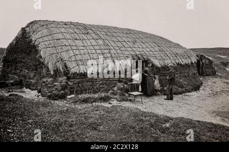 Una vista dei primi anni '20 di un tappeto erboso (torba) costruito, cottage con tetto di paglia nella contea di Derry (Londonderry), Ulster, Irlanda del Nord. La famiglia, può essere visto radunato intorno alla porta. Originariamente fotografato da Clifton Adams (1890-1934) per 'Ireland: The Rock Whence i was hewn', una rivista nazionale di geografia dal marzo 1927. Foto Stock