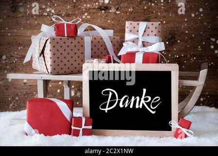 Lavagna con il tedesco Calligraphy Danke significa Grazie. La slitta con un regalo di Natale e regali. Sfondo di legno con la neve e i fiocchi di neve Foto Stock