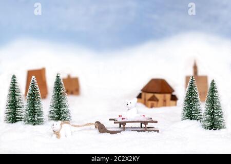 Natale greeting card modello. Focus su orso polare tira una slitta con un altro portano su di esso attraverso la neve contro il giocattolo sfocata alberi, case e sn Foto Stock