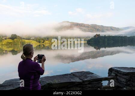 Fotografando il Mist di mattina presto sopra il lago di Grasmere, Lake District, Cumbria, Regno Unito Foto Stock