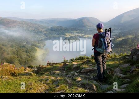 Walker godendo della vista sul lago Grasmere da Loughrigg cadde in una mattinata estiva misty, Lake District, Cumbria, UK Foto Stock