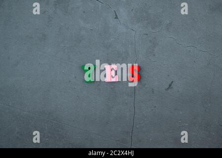 Il variopinto Sì parola è fatta di lettere in legno su un grigio muro intonacato sfondo Foto Stock