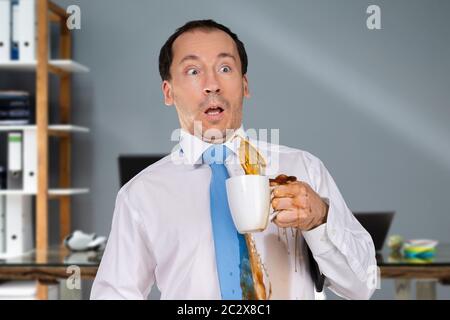 Uomo Che Lancia Il Caffè Sulla Sua Camicia In Ufficio Foto Stock