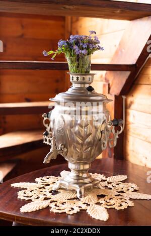 Samovar in metallo antico e bouquet di fiori blu su sfondo di legno Foto Stock