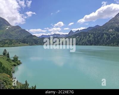 Im Vordergrund des Bildes ist der Kopssee, er Hat türkisfarbiges Wasser. Der Stausee Liegt in den österreichischen Alpen. Im Hintergrund sind die Berg Foto Stock