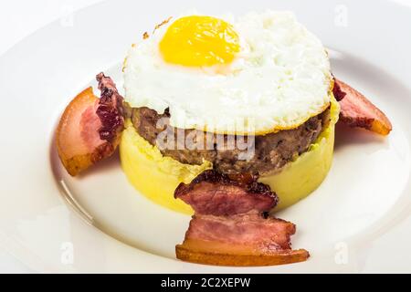 colazione a base di omme. uova fritte e polpettine di carne sulla patata schiacciata, decorata con pancetta. cibo isolato su sfondo bianco. vista ravvicinata Foto Stock