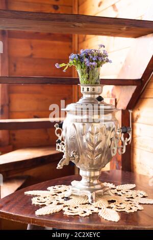 Samovar in metallo antico e bouquet di fiori blu su sfondo di legno Foto Stock