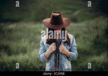 La ragazza da sola in campo in serata tiene su una giacca di denim come se congelato sul cappello del cowboy della testa fuori Foto Stock