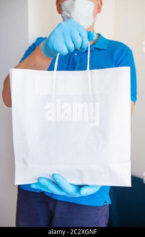 Servizio di consegna a domicilio, ragazzo mascherato e guanto consegna un sacchetto di cibo alla porta. Distribuzione senza contatto durante una pandemia di virus. Primo piano. Foto Stock