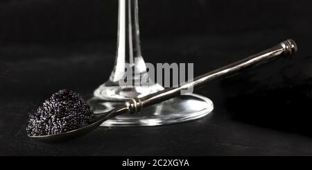 Il caviale nero su un cucchiaio con un bicchiere di champagne, una panoramica di close-up su sfondo nero Foto Stock