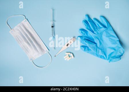 Guanti in lattice blu su sfondo blu con pillole, maschera medica, termometro e siringa. Il concetto di salute e di autocontrollo per virus e e Foto Stock