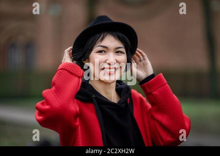 Ragazza orientale in un cappotto rosso elegante e cappello nero in un ambiente urbano Foto Stock