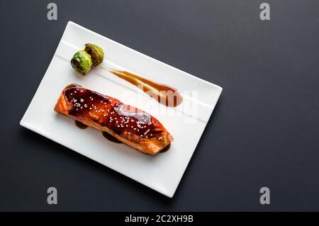 Cucina giapponese ispirato a piatti fatti di filetto di salmone alla griglia smaltato in deliziosa salsa teriyaki (base di salsa di soia) e germogli di Bruxelles su piatto bianco. Foto Stock